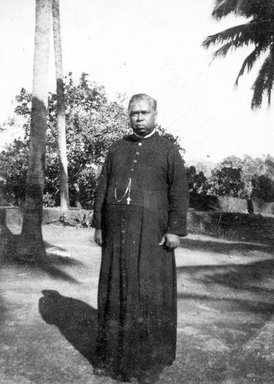 Full length historical photograph of Fr. Charles M. Fernandez standing outdoors in classical cassock attire